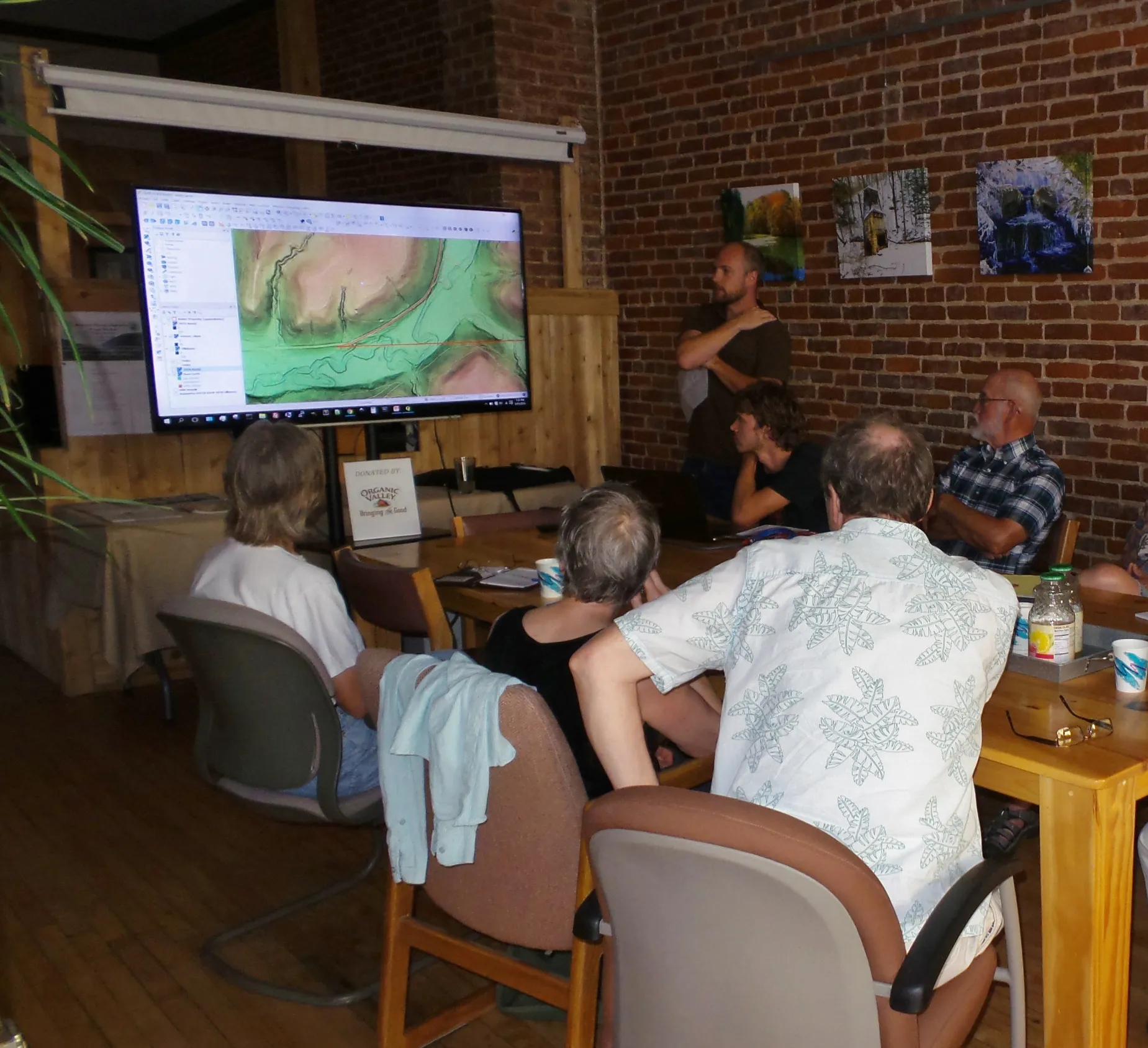 Photo of people at a large table looking at slideshow with hillshade map on it.